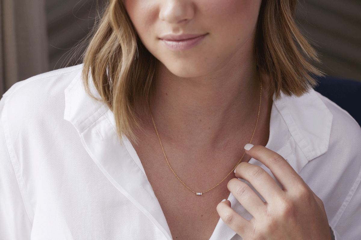 Woman wearing thin gold chain necklace with diamond baguette and white shirt