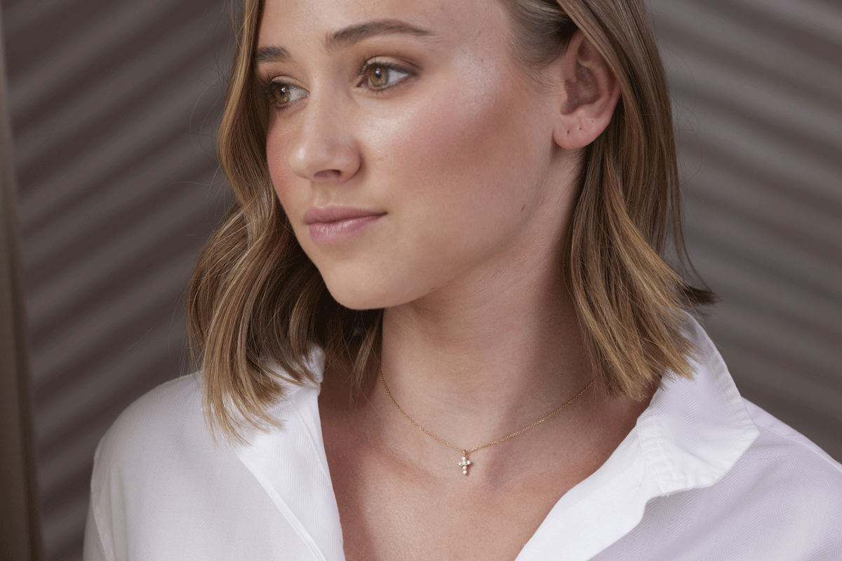 Girl wearing a thin gold chain necklace with diamond cross charm