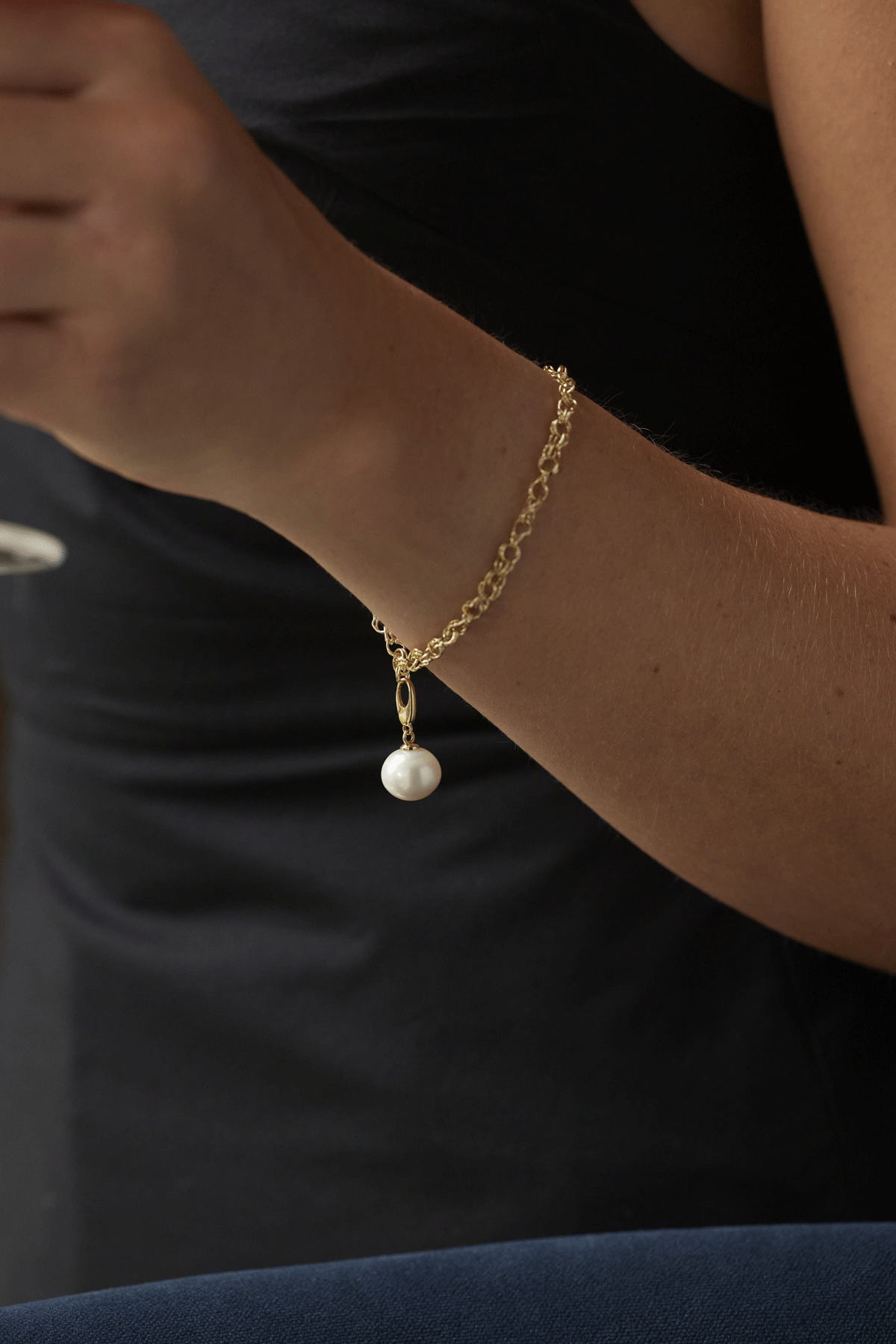 Woman's wrist with gold chain charm bracelet with singular pearl charm