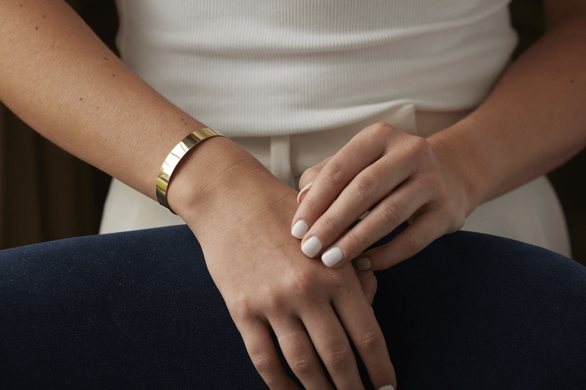 Woman's hands wearing a thick gold cuff bracelet