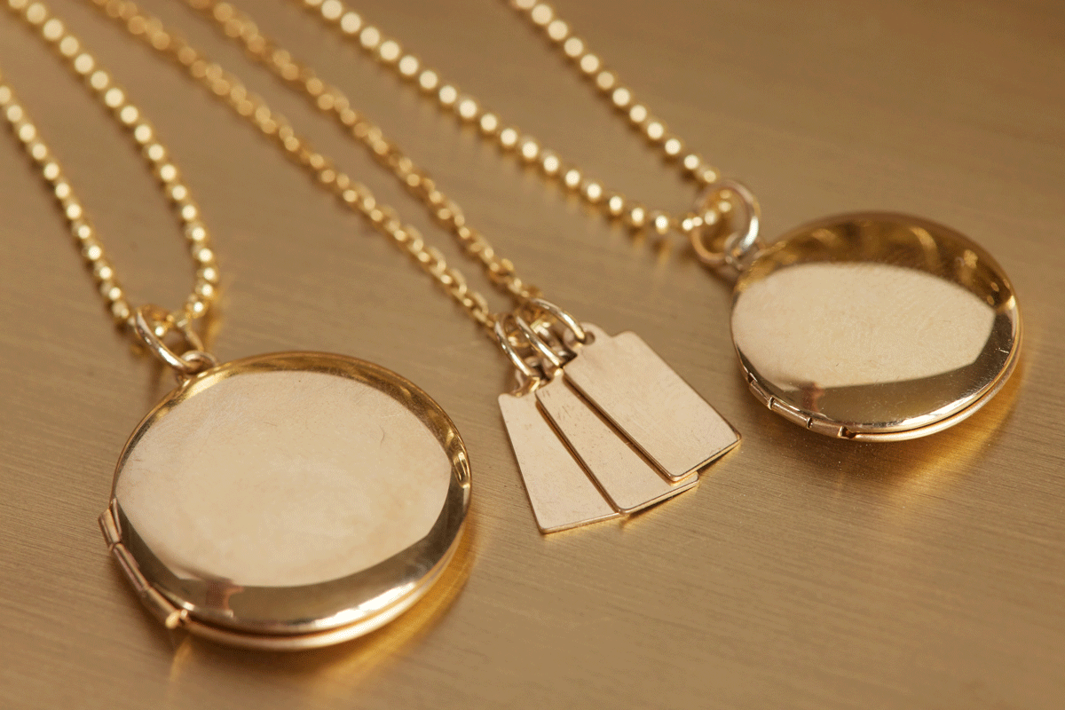 Detail close up of two locket pendants and tiny gold tags on gold chains