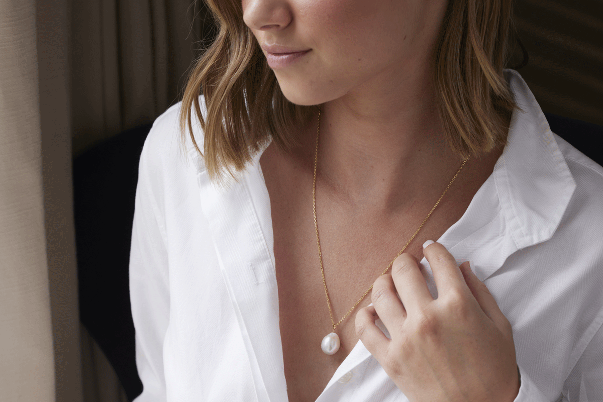 Woman wearing a white shirt with thin gold chain and pearl drop pendant