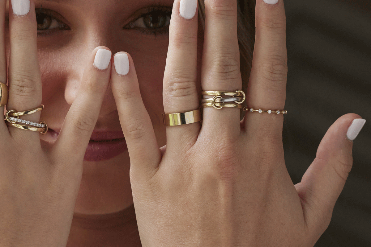 Woman with her hands in front of her face showing all of her different gold ring styles